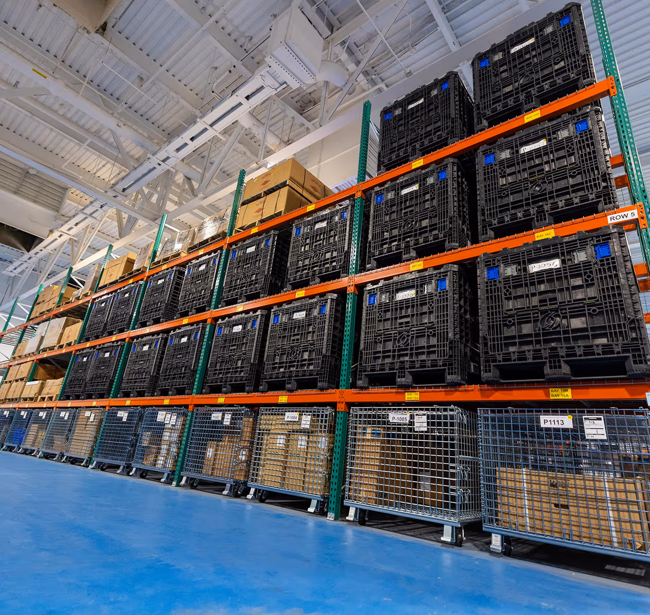 Warehouse racks filled with black crates and metal cages holding boxes on a blue floor.